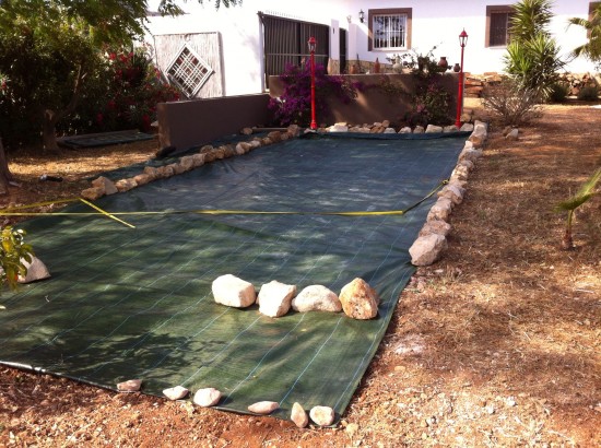 Het begin: grond gelijk gemaakt, geharkt en grote stenen verwijderd, worteldoek gelegd,;12x 3 mtr en dan komen de zandzakken voor de deur.....